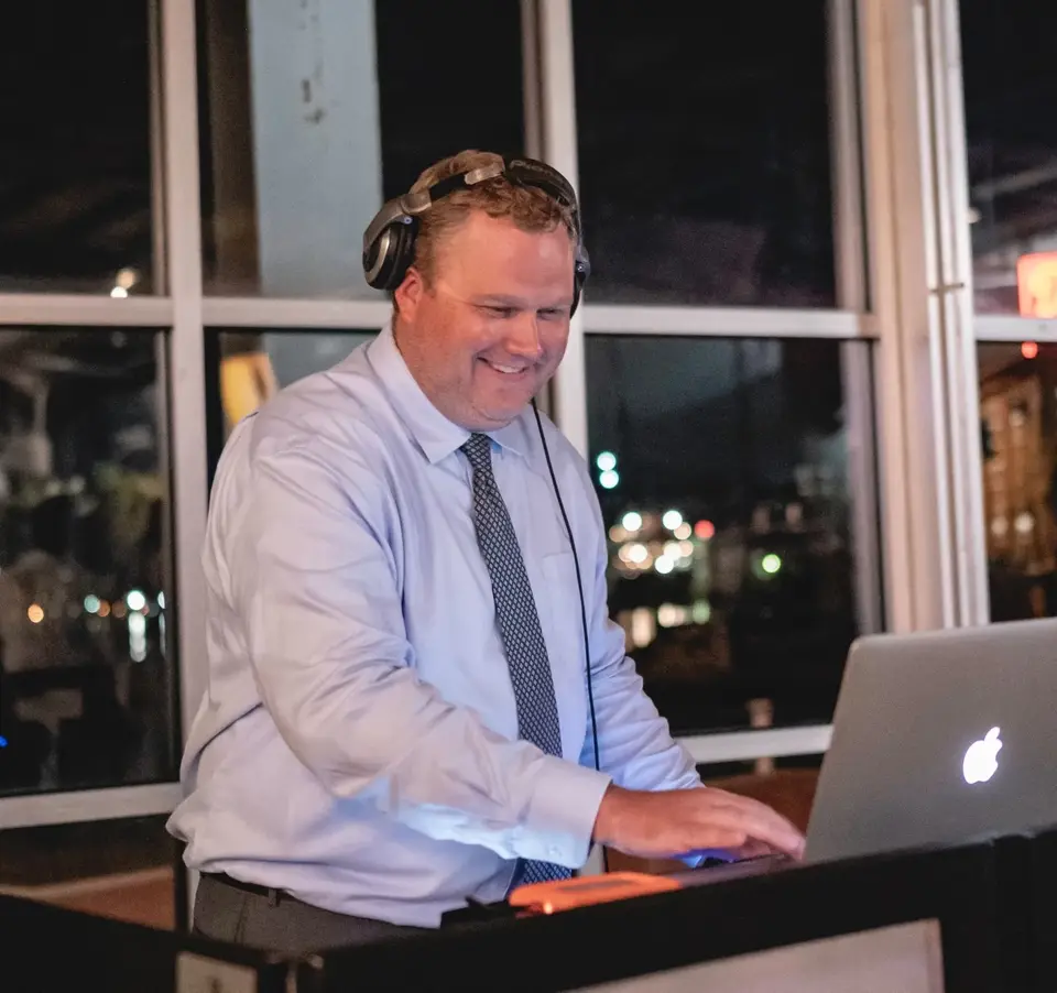 DJ in a light blue shirt and tie wearing headphones and working on a laptop