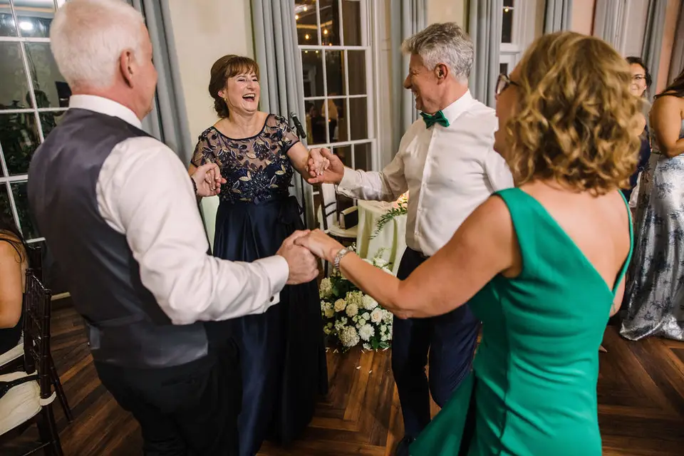 Guests holding hands and dancing in a circle on the dance floor, including a woman in a green dress