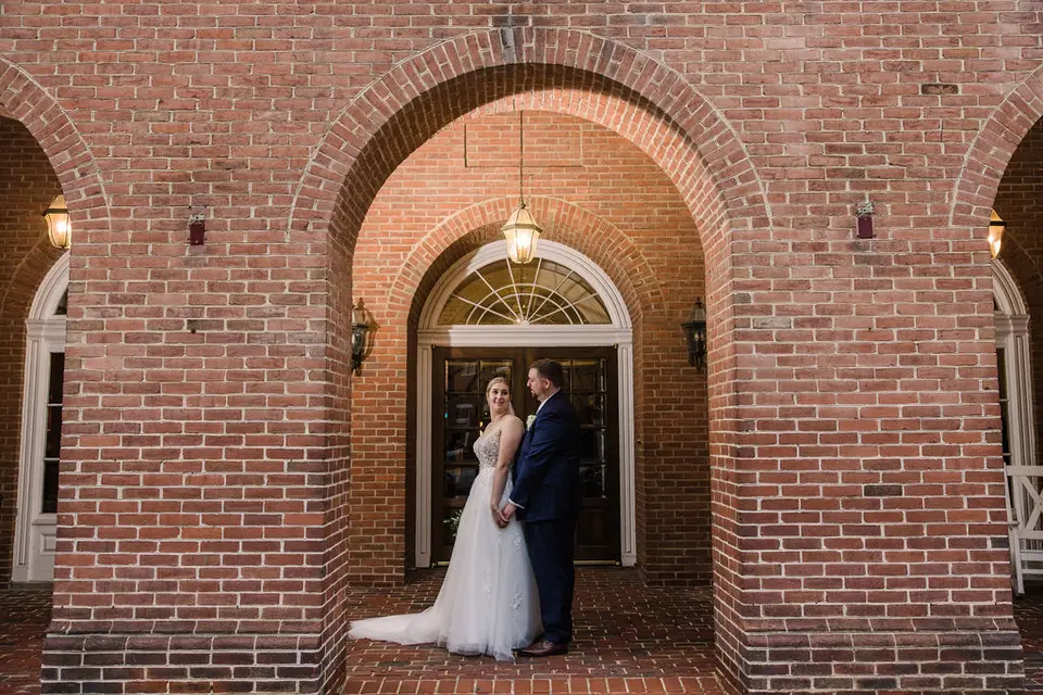 Bride and groom standing close together under tall brick archways in front of a double door