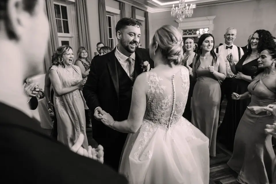 Black and white photo of the groom and bride laughing as they dance among guests