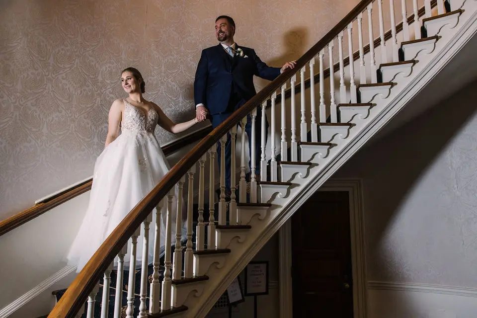 Bride in a lace gown and groom in a navy suit standing on a wooden staircase