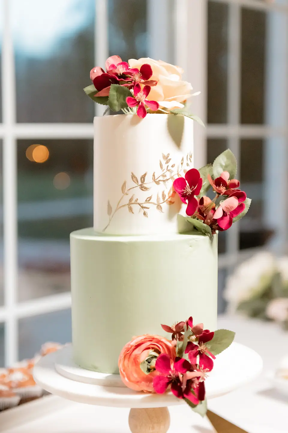 Two tier wedding cake in white and sage green topped with burgundy and peach flowers