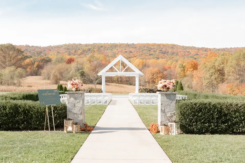 Ceremony site with a white gazebo, white chairs and a welcome sign facing autumn hills