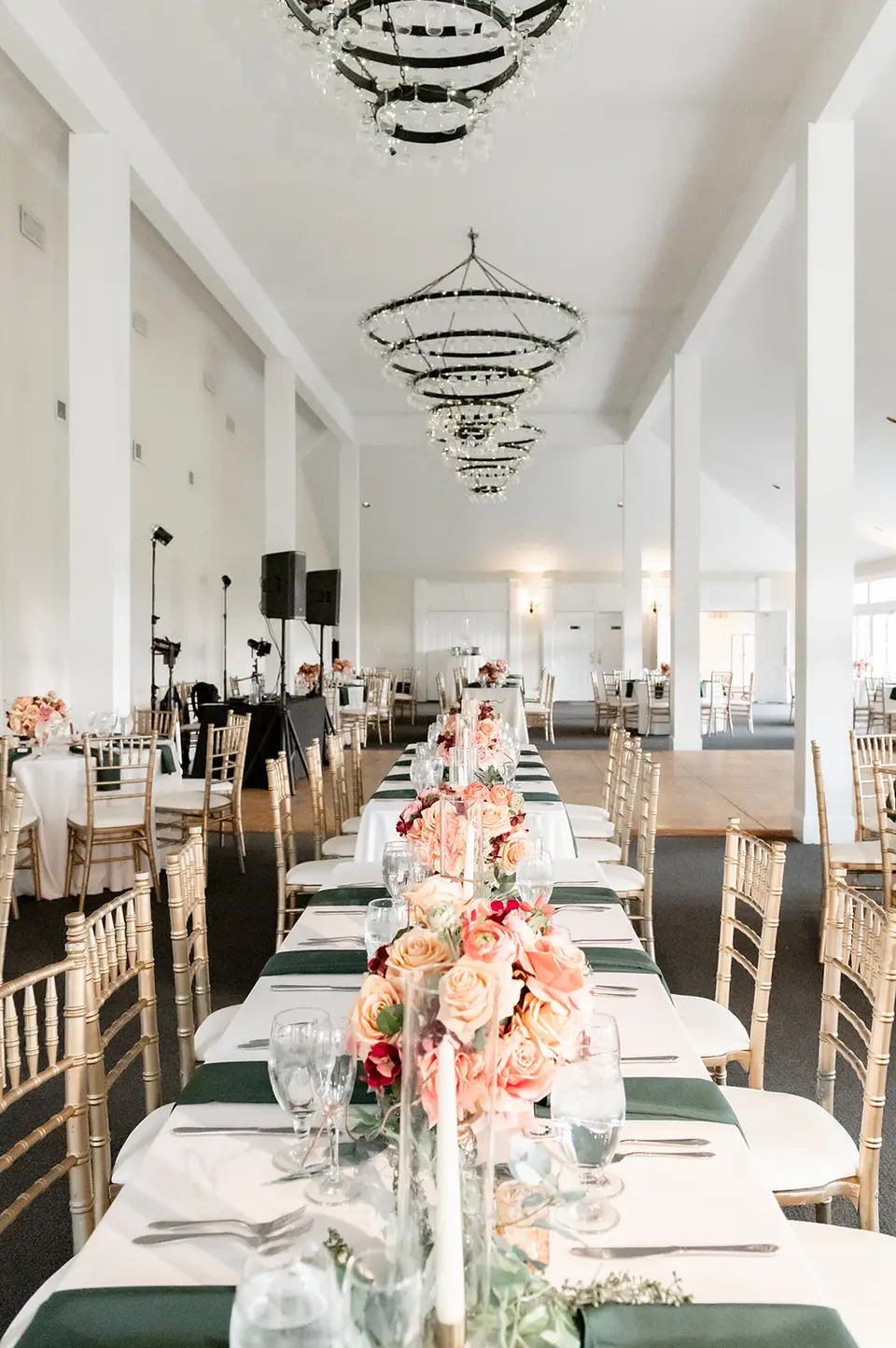 Long reception table with peach roses, green napkins and gold chairs in a large hall