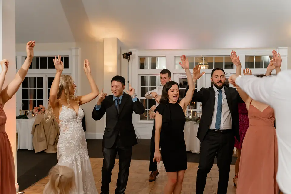Bride and wedding guests dancing with arms raised on a parquet dance floor