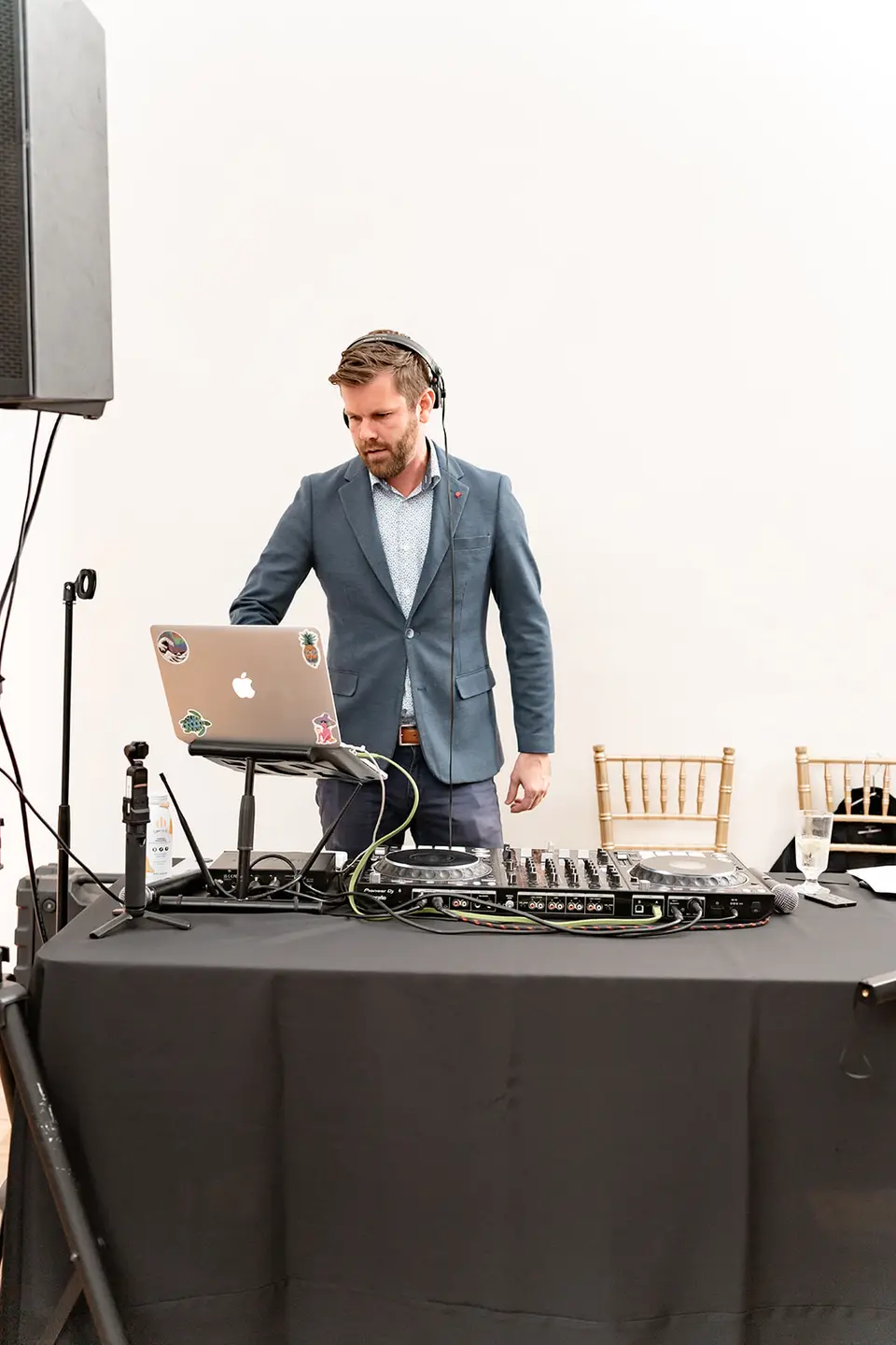 DJ in a blue blazer and headphones working at a laptop and controller on a draped table