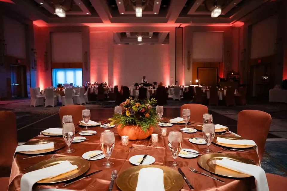 Ballroom reception with an orange-lit wall, a pumpkin centerpiece and gold chargers on a round table