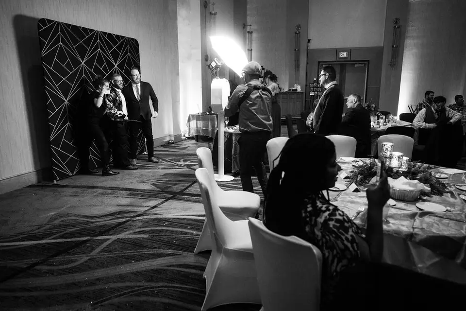 Black and white view of a photo backdrop and a reception room with guests and white chair covers