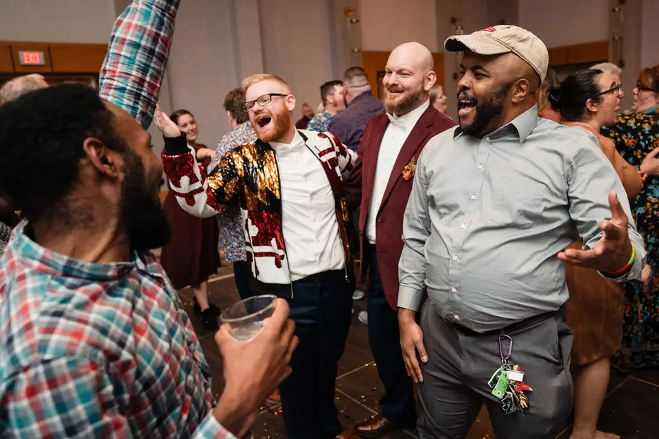 Wedding guests cheering and dancing around a groom in a patterned jacket