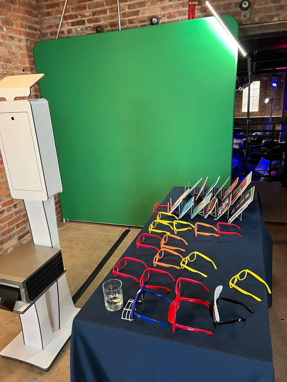Photo booth, green screen backdrop and table of colorful glasses on display in a brick room