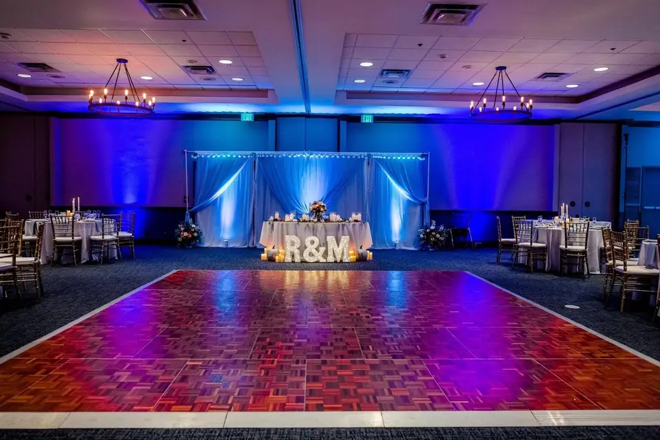 Empty reception ballroom with blue lighting, a parquet dance floor and a sweetheart table with an R&M sign