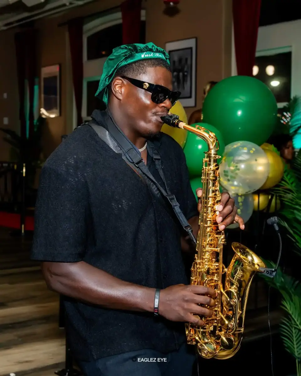 Saxophonist in a green bandana and sunglasses playing a gold saxophone beside green balloons