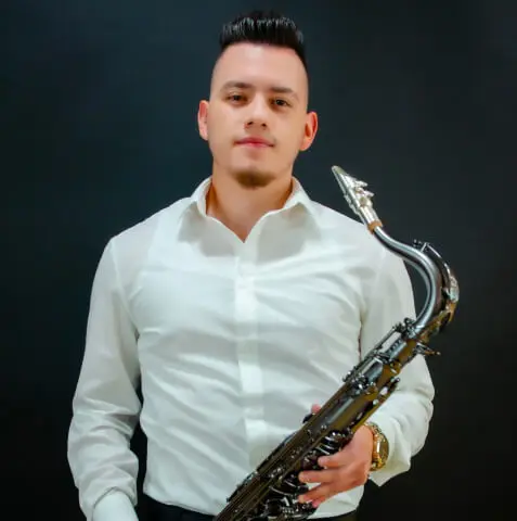 Young man in a white shirt holding a silver saxophone against a dark background