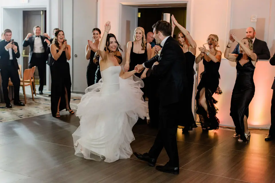 Bride dances with the groom while bridesmaids and guests clap and cheer on the dance floor