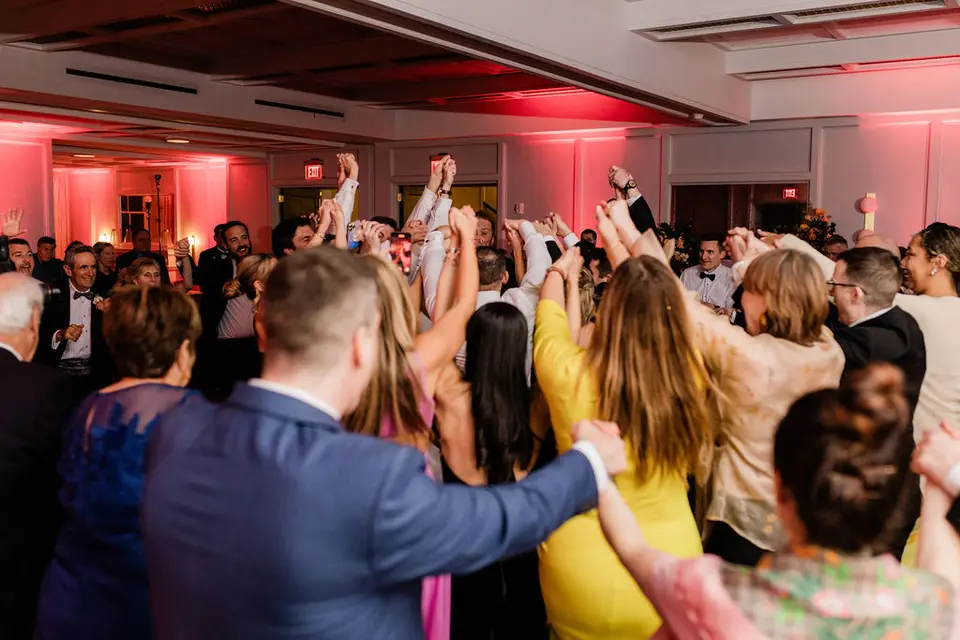 Guests dancing with arms in the air in a ballroom lit with pink uplighting