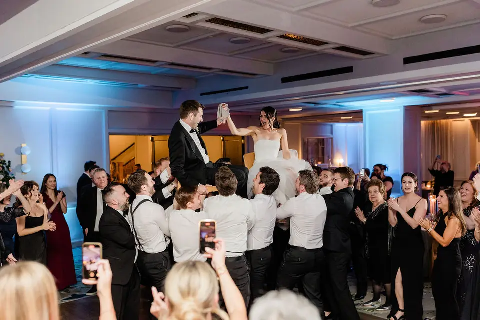 Groom lifted on a chair above the crowd of cheering guests during a hora at the reception
