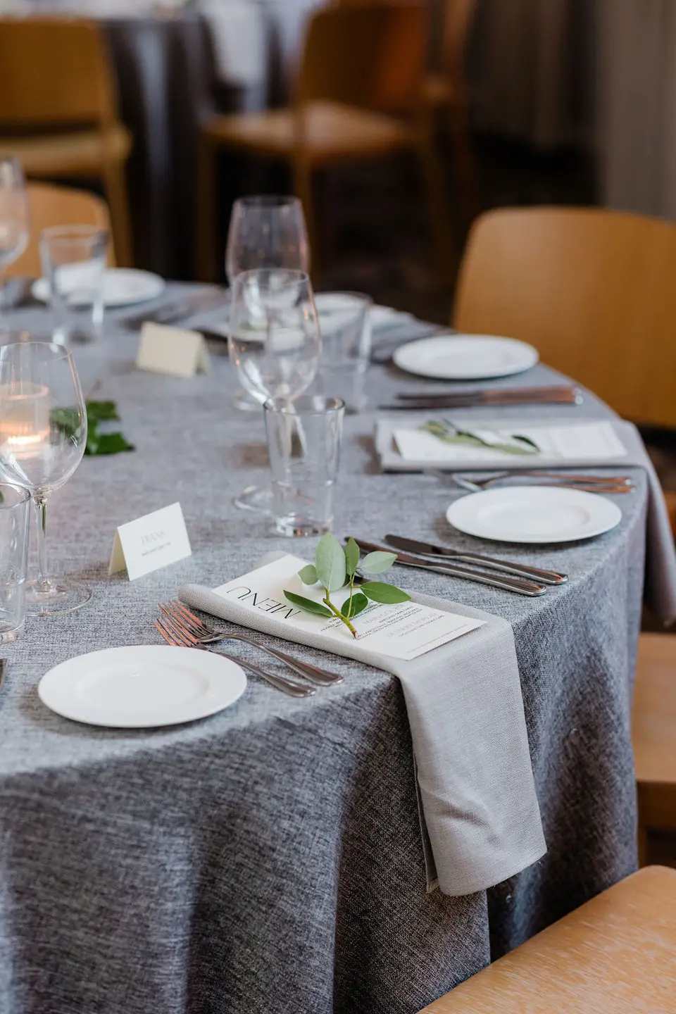 Round reception table with gray linen, white plates, a menu card, and a sprig of greenery