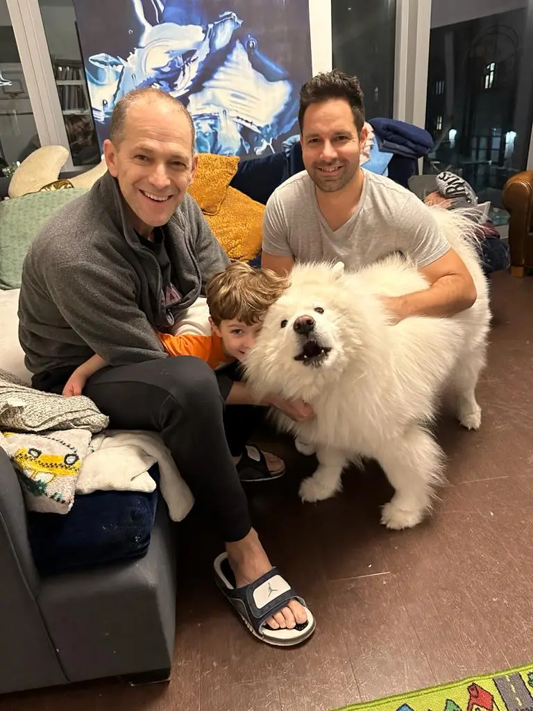 Two men sitting on a couch with a young boy and a large white fluffy dog