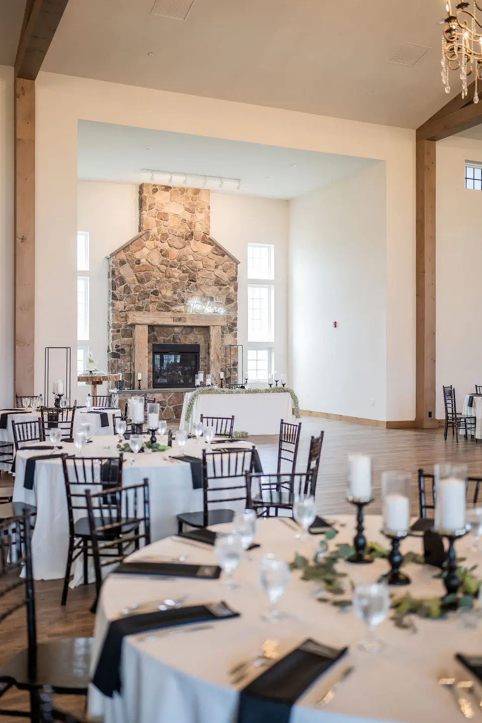 Reception hall set with round tables, candles and black napkins in front of a stone fireplace