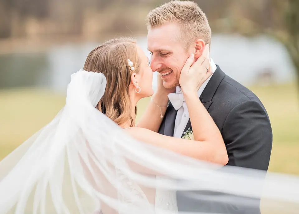Close-up of the bride and groom smiling at each other as her veil blows across the frame