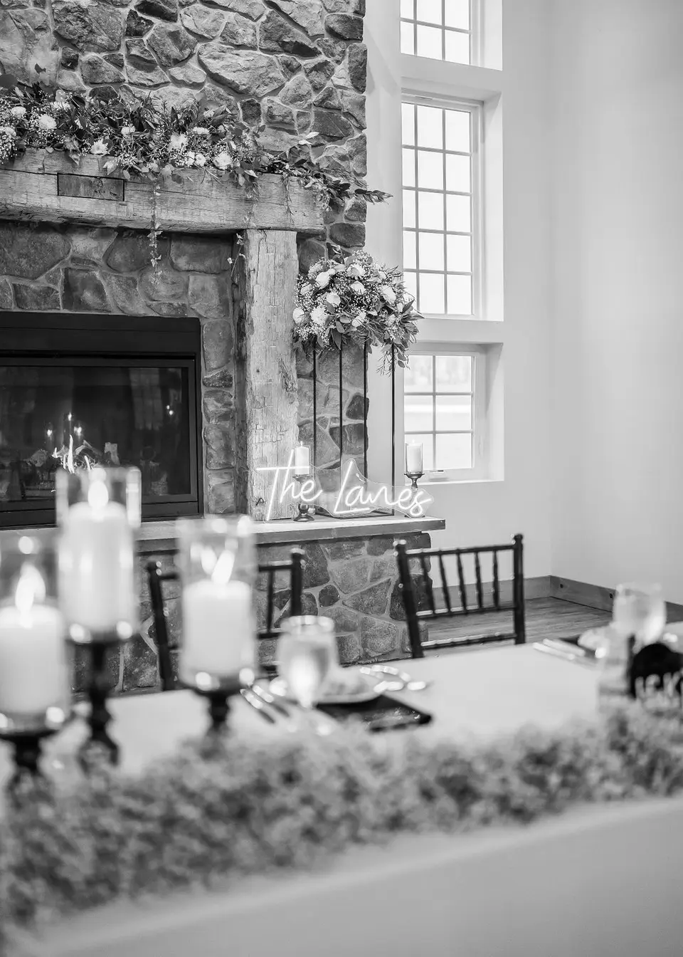 Black and white view of a stone fireplace with a neon sign reading The Lanes and candles in the foreground