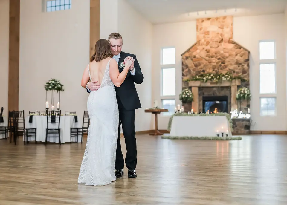 Bride and groom sharing a first dance on a wood floor in front of a stone fireplace