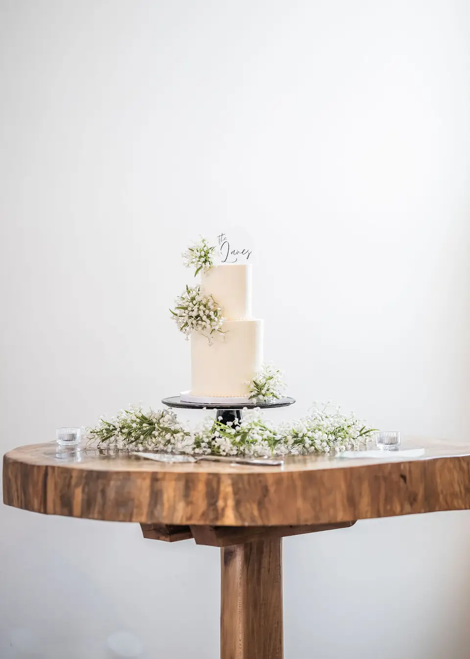 Small two-tier white cake with baby's breath on a rustic wooden slice table