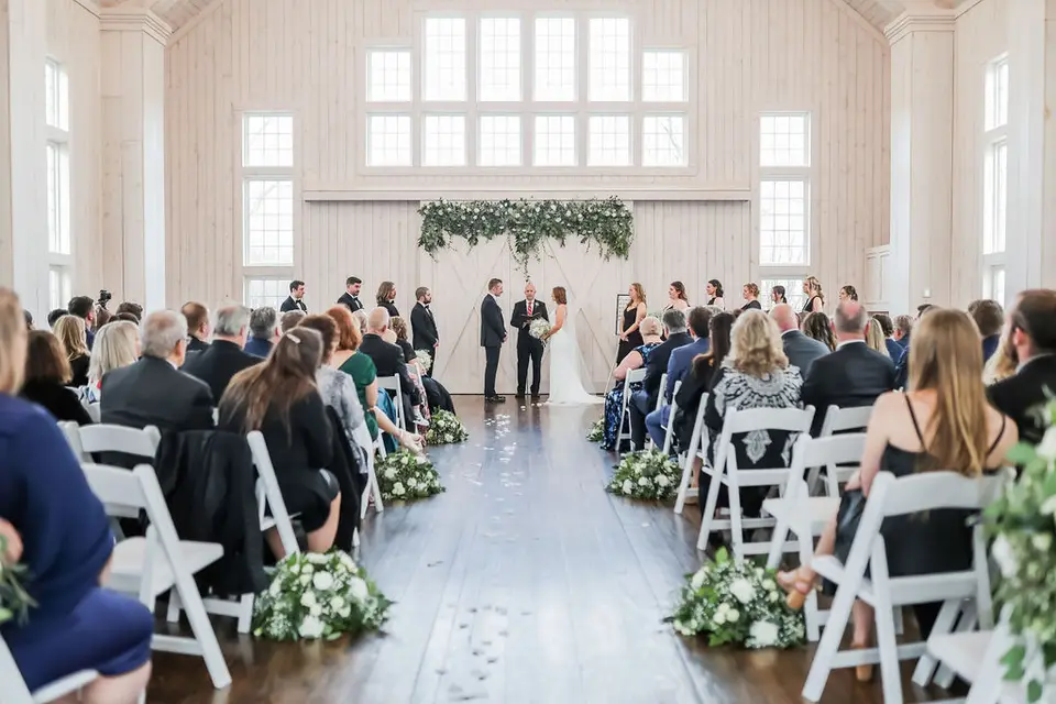 Couple at the altar during a ceremony in a bright hall with guests seated in white chairs