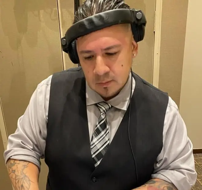 DJ in a black vest, gray shirt and striped tie wearing headphones on his head