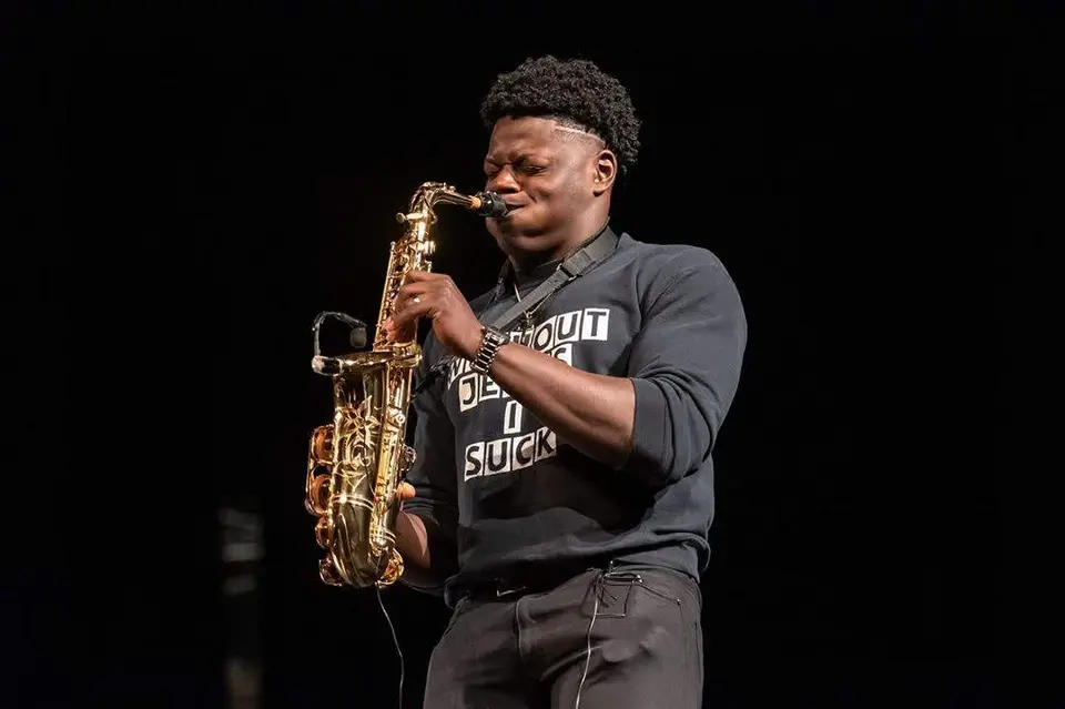 Saxophonist in a dark sweatshirt playing alto sax on a dark stage