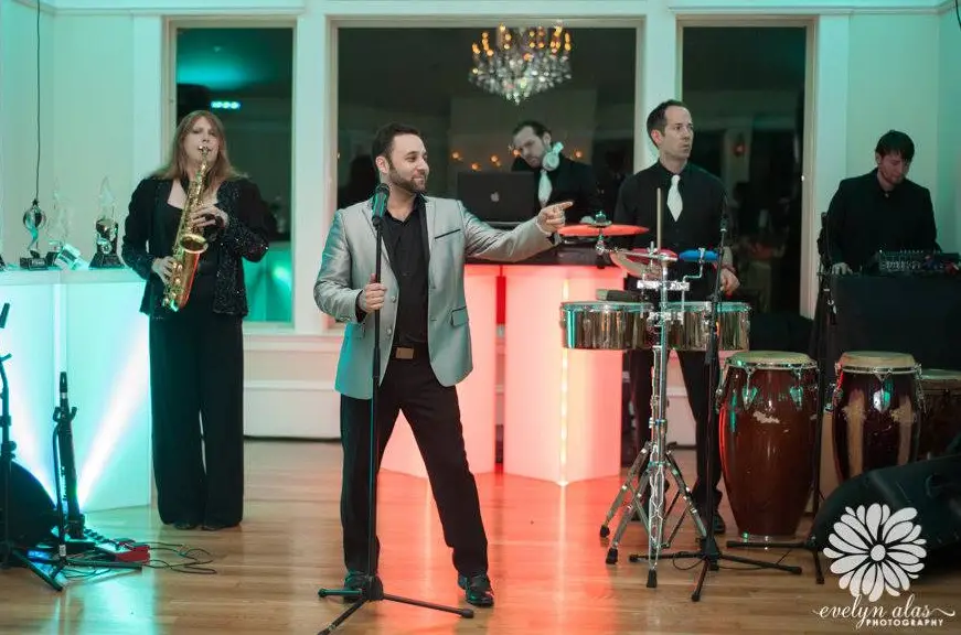 Live band with a sax player, percussionists and a singer in a gray jacket on a lit dance floor