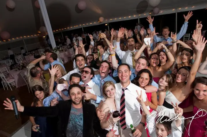 Crowd of wedding guests cheering and posing around the DJ taking a selfie under a tent