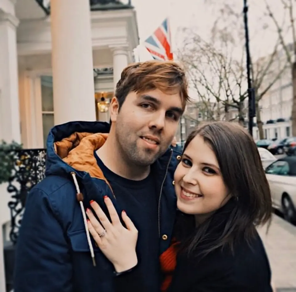 Smiling man and woman posing close together on a London street with a Union Jack flag behind them