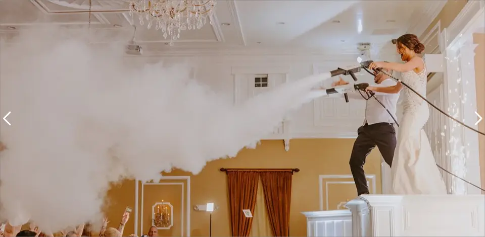 Bride and groom on a platform firing low smoke cannons that fill a ballroom with fog