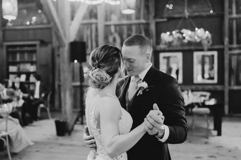 Black and white photo of a bride and groom dancing close together in a barn