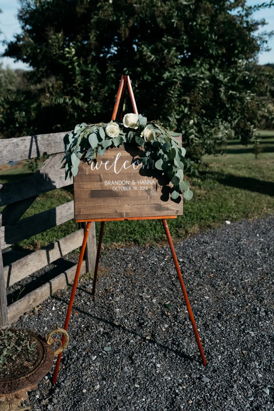 Wooden welcome sign with eucalyptus and white roses on an easel for Brandon and Hanna's wedding