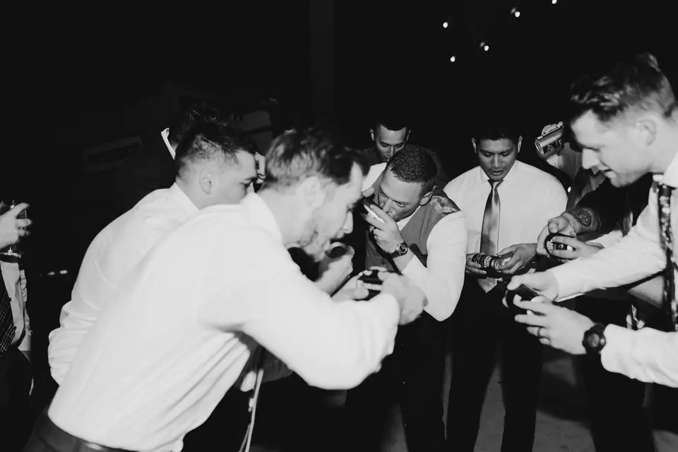 Black and white photo of groomsmen huddled together on the dance floor holding drinks