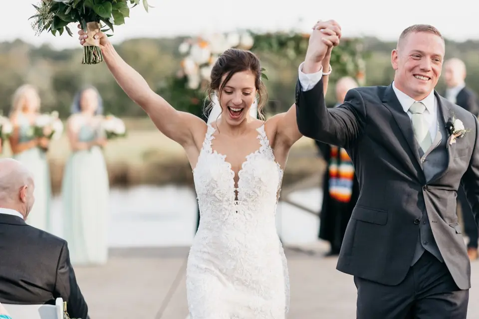 Bride and groom raise their arms and laugh while walking up the aisle after the ceremony