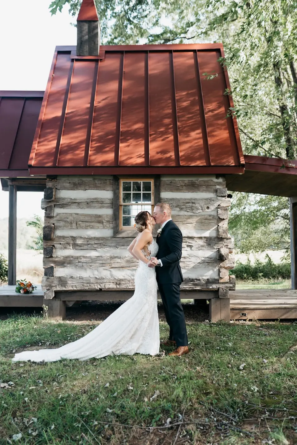 Bride and groom kissing in front of a small log cabin with a red metal roof