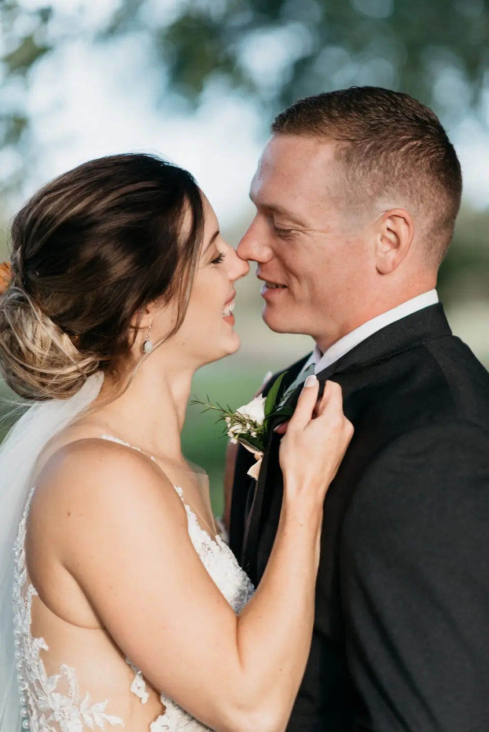 Bride and groom smiling with their foreheads together outdoors, bride adjusting his lapel