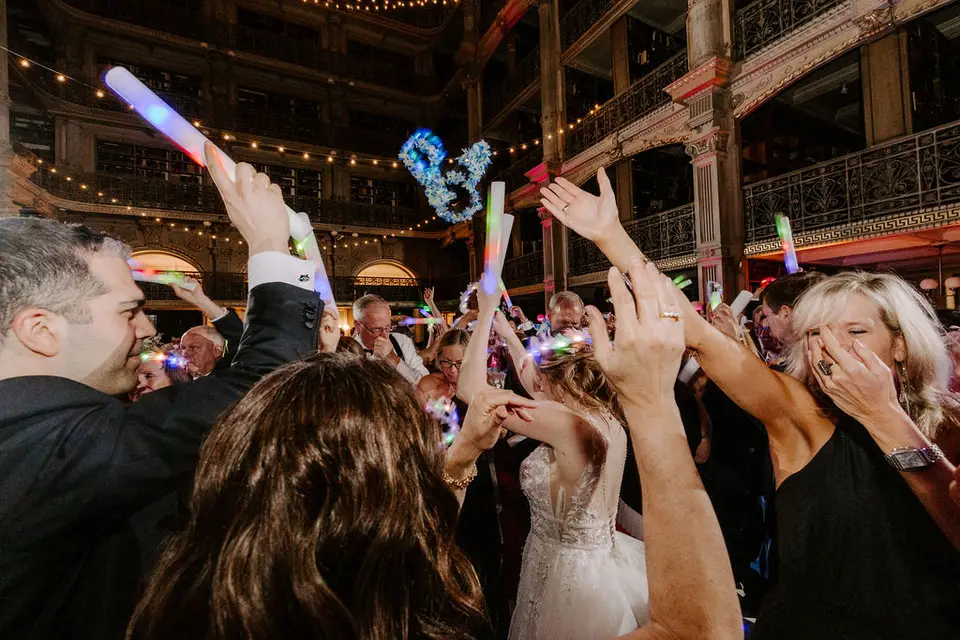Wedding guests holding glow sticks and waving their arms on a crowded dance floor in the library