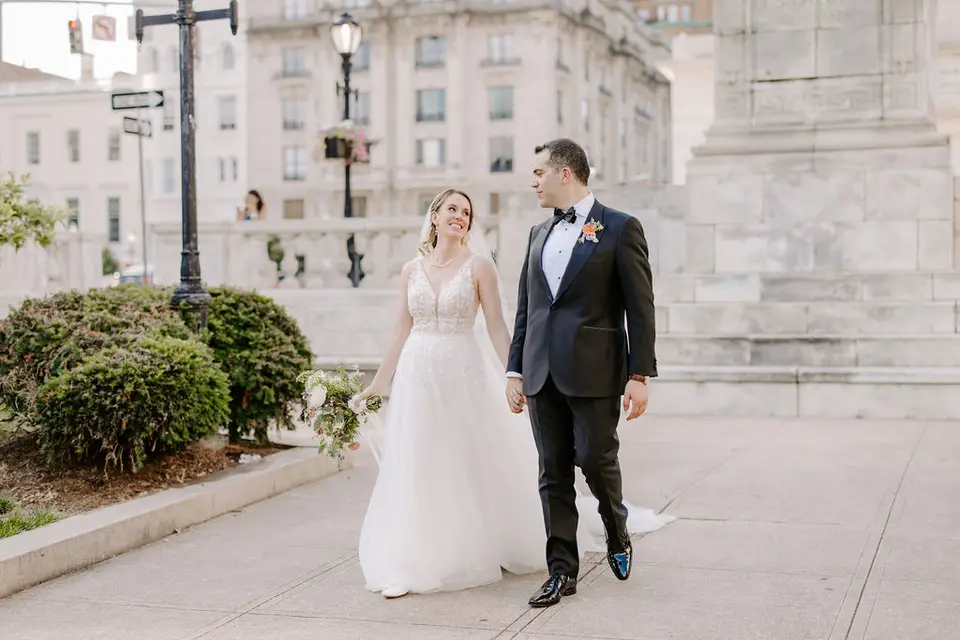 Bride and groom walking hand in hand on a city sidewalk near stone steps