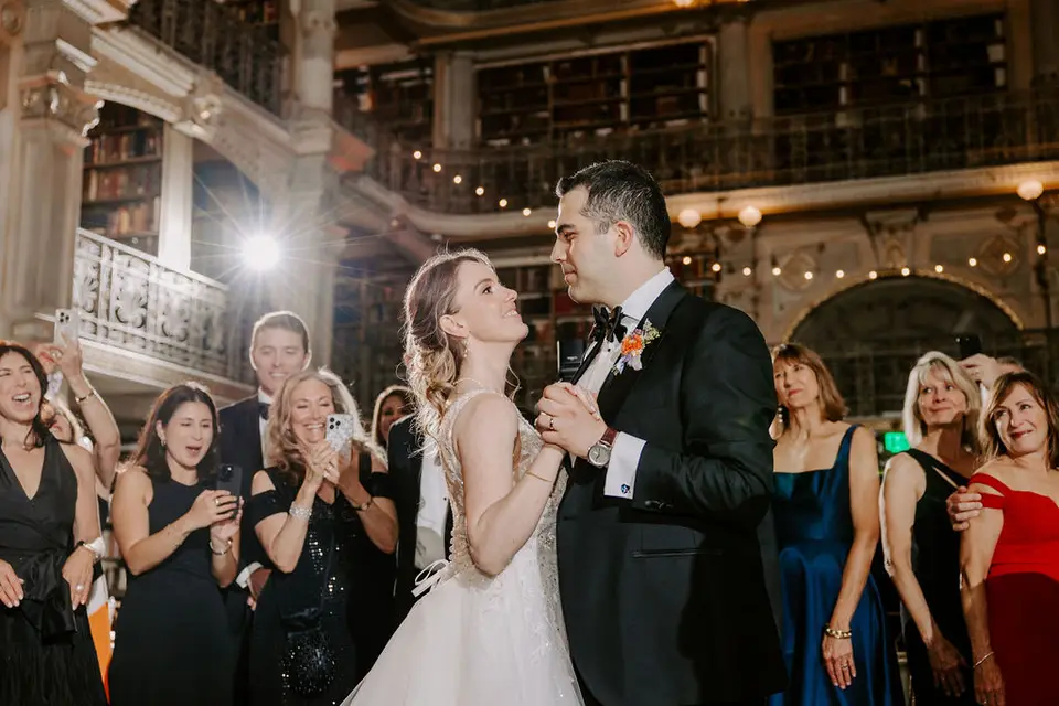 Bride and groom dancing together in the library ballroom while guests watch and film