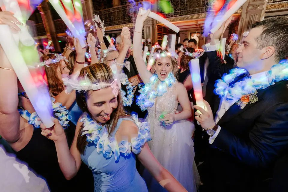 Bride and guests in glowing flower leis dancing with glow sticks on the dance floor