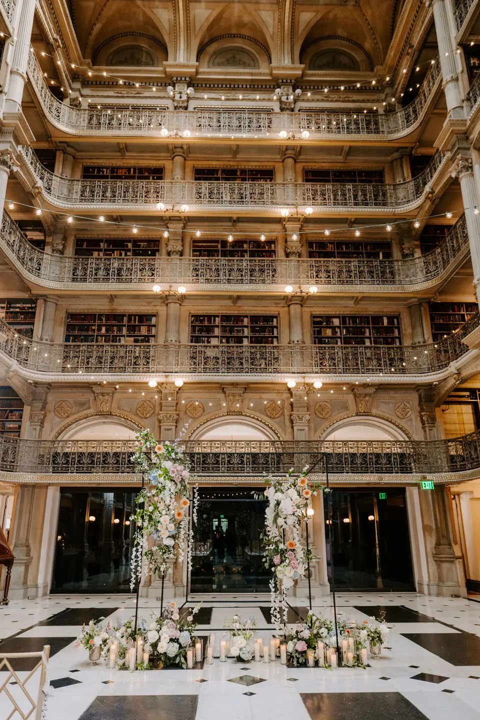 Tall George Peabody Library atrium with balconies and floral arrangements on the floor below