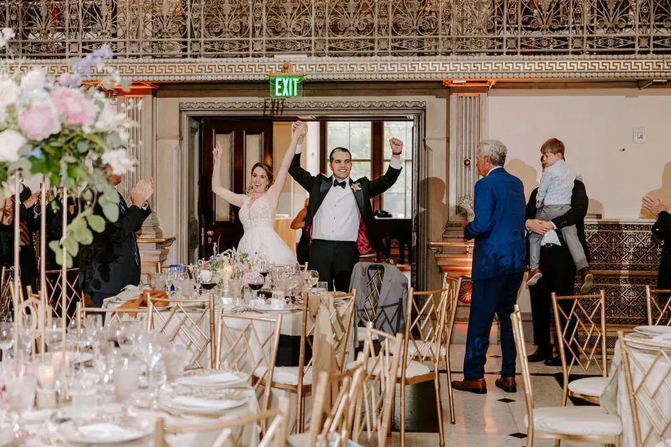 Bride and groom raising their arms in celebration as they enter the reception past decorated tables