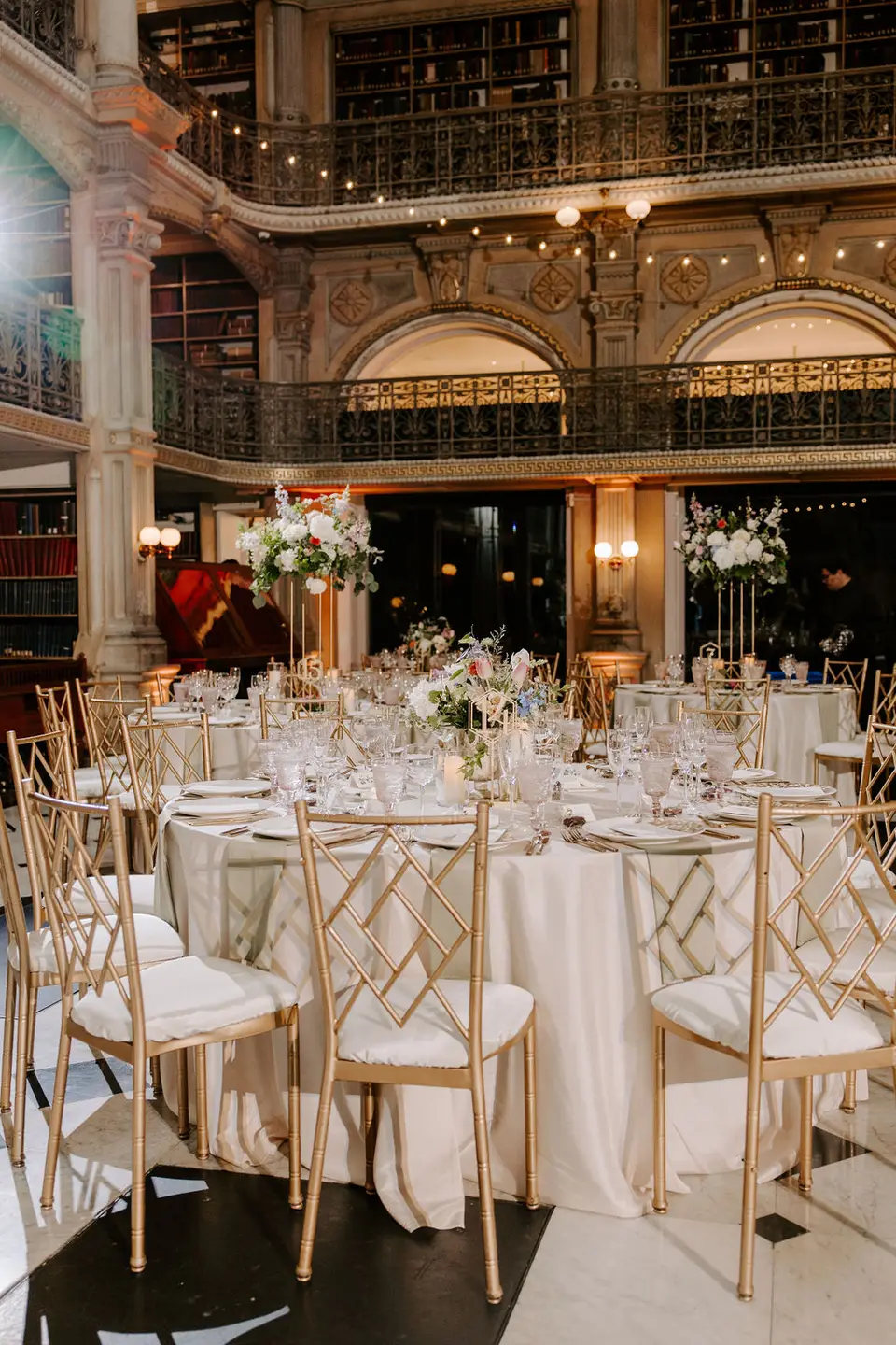 Round reception table with gold chairs and white and pink floral centerpiece inside the library