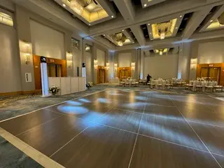 Empty hotel ballroom with a wood dance floor, DJ booth in the distance and tables set at the back