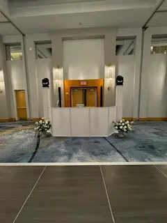 White-fronted DJ booth with speakers and flower arrangements set up beside a dance floor