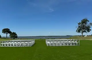 Rows of white folding chairs set up on a lawn overlooking the water for an outdoor ceremony